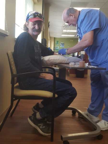 Man with lung cancer looks away as nurse inserts needle into his arm