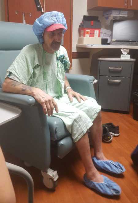 Man with lung cancer sitting in chair in hospital room wearing gown, 