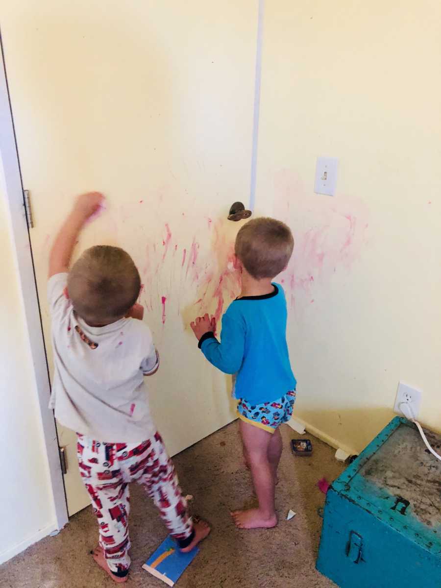 Two toddler boys coloring with red marker on white door