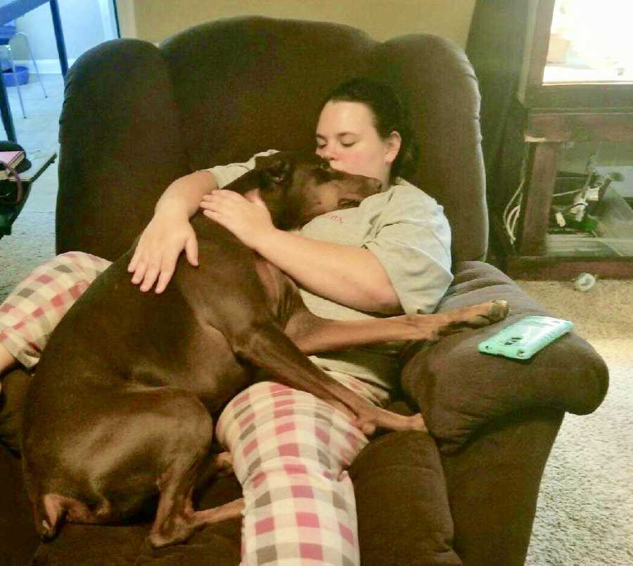 Woman sits in recliner with brown dog on her lap