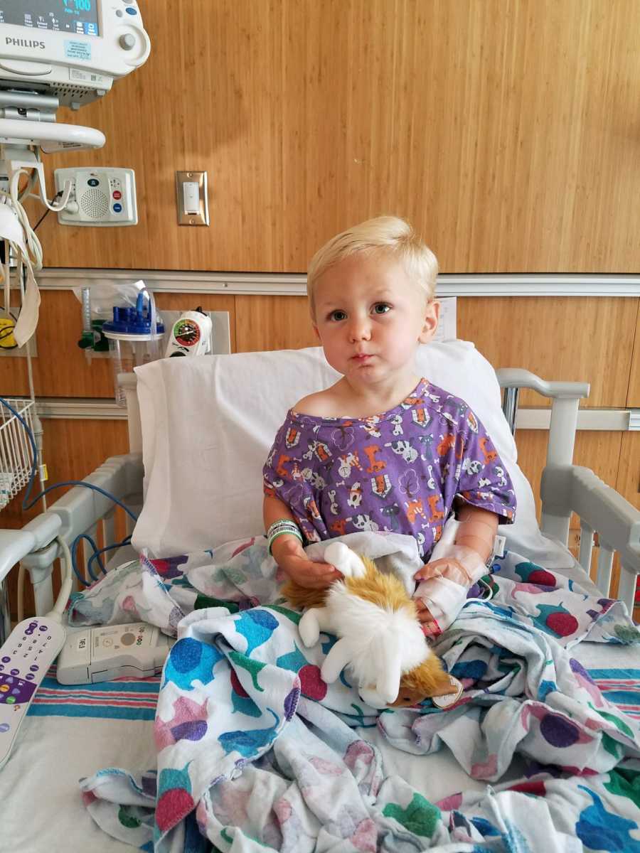 Toddler with heart defect sits up in hospital bed holding stuffed animal