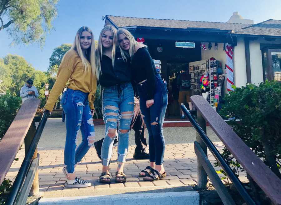 Three teens whose father passed away stand smiling beside outdoor steps