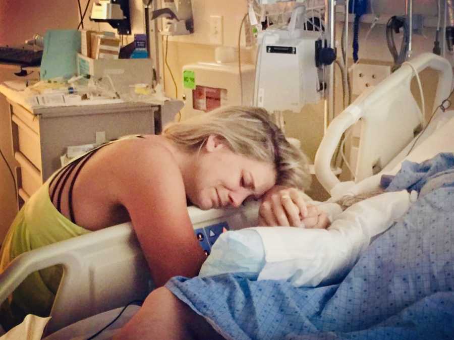 Woman leans over hospital bed holding mothers hand who abuses drugs