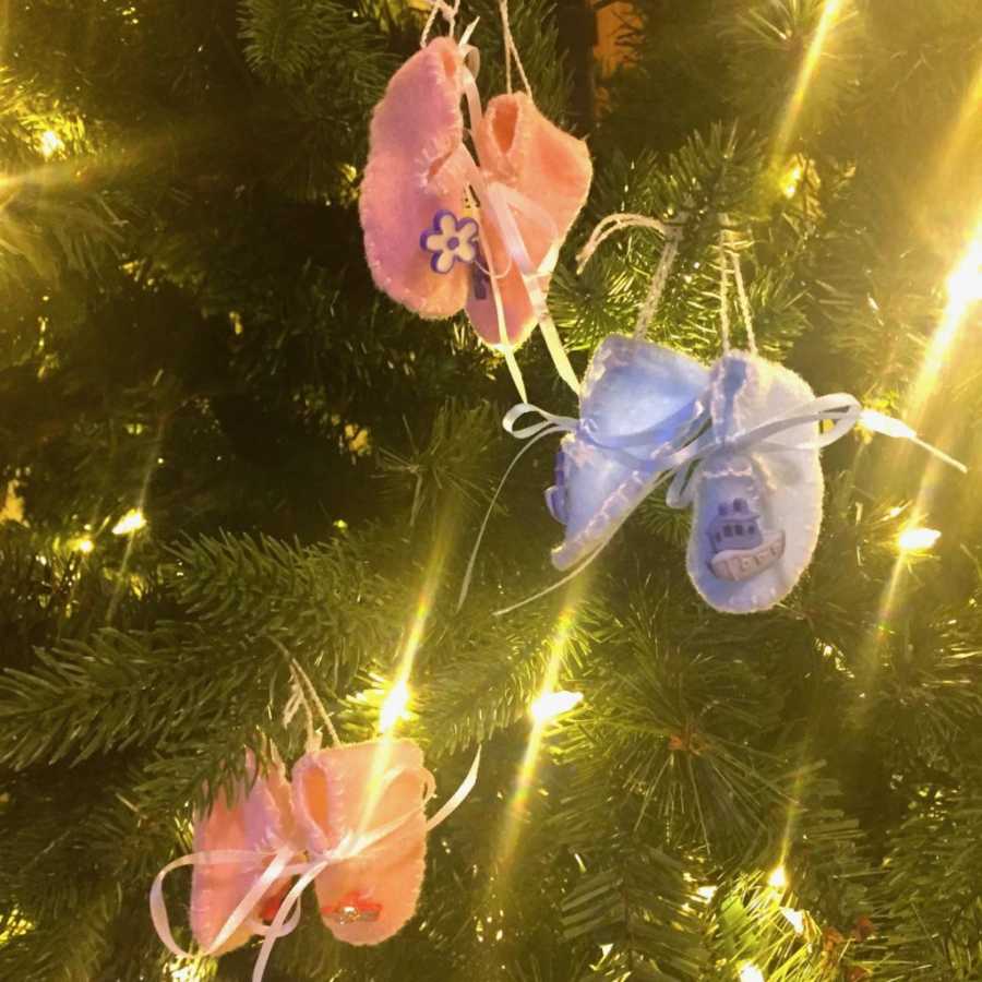 Two pink baby slippers and pair of blue slippers tied to Christmas tree for triplets