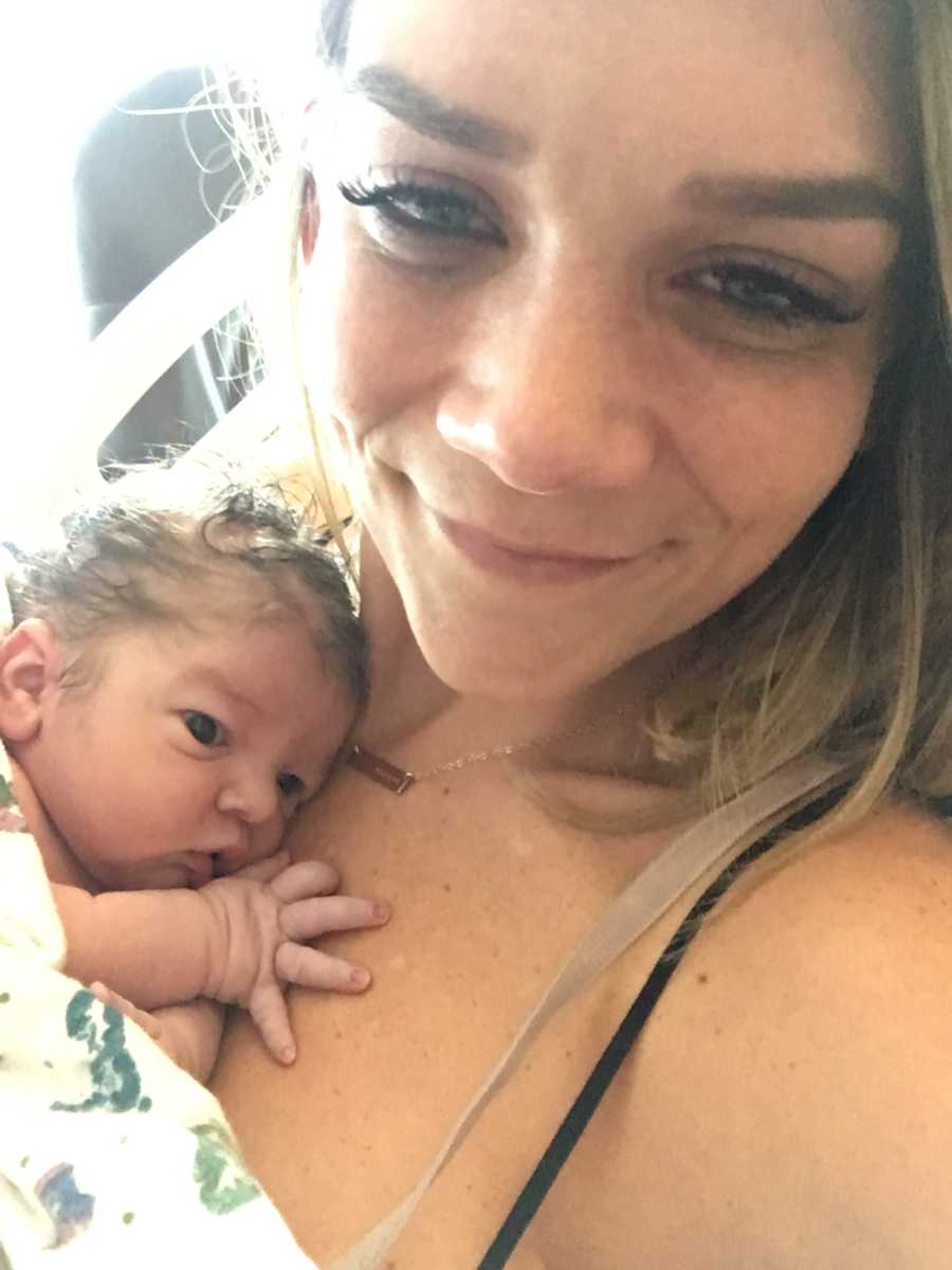 Mother smiles in selfie with her adopted child laying on her chest
