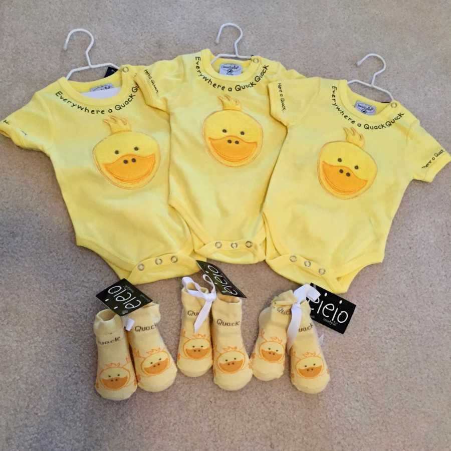 Three onesies with duck faces on them and duck slippers beside them for triplets 