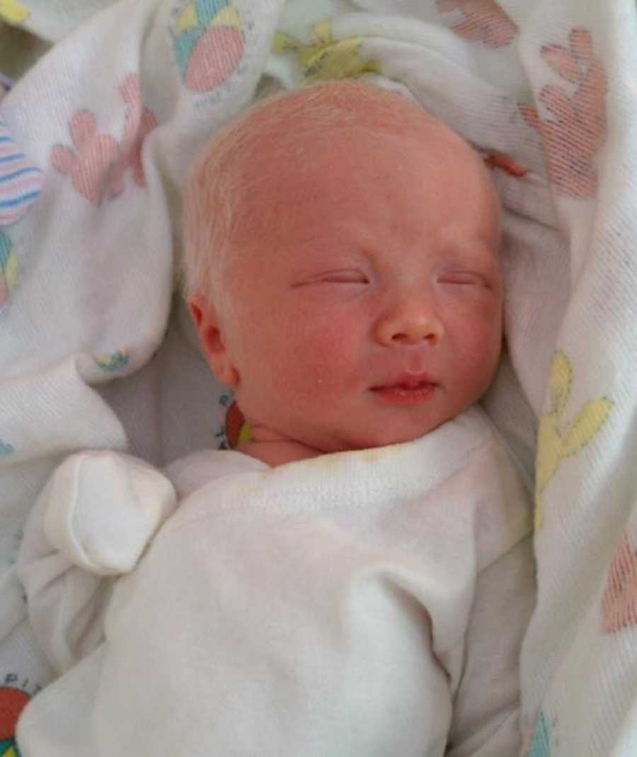 Newborn baby with bright white hair lays asleep in white onesie