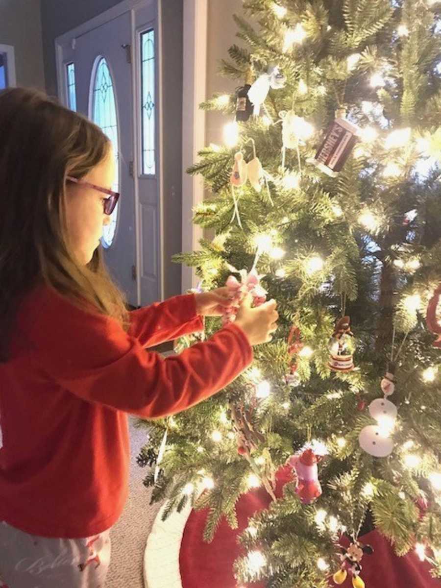 Young girl who is the only survivor of triplets touches ornament on Christmas tree