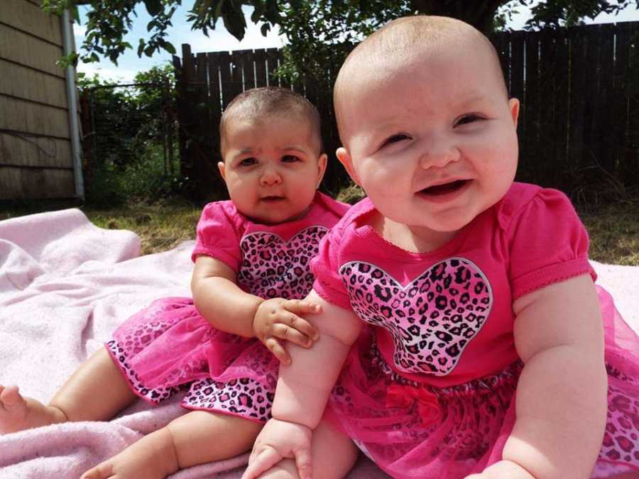 Baby girls in matching outfits whose mothers are cousins sit on pink blanket outside