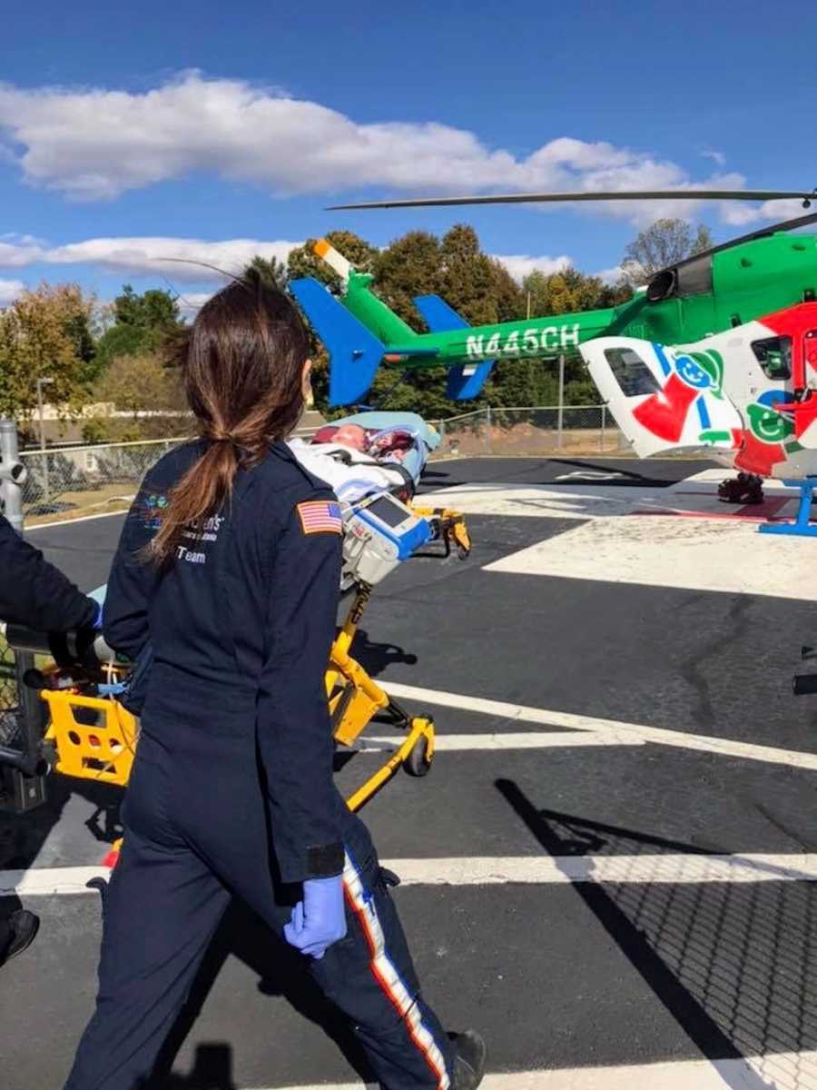 Baby on stretcher being pushed by EMT's towards helicopter