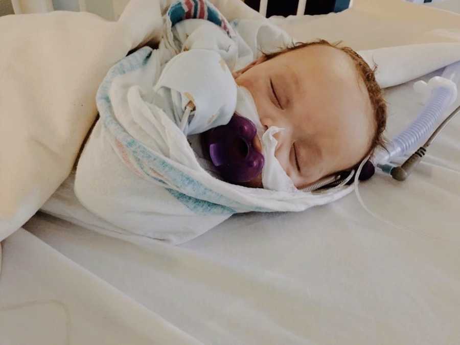 Baby with RSV sleeping in PICU crib wrapped in blankets