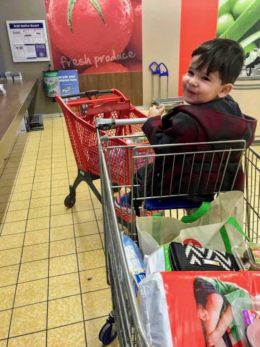 Young boy sitting in shopping cart looking over his shoulder in store