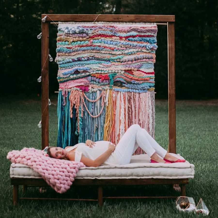 Woman who struggled with fertility lays on bench outside pregnant with crochet blanker hanging behind her