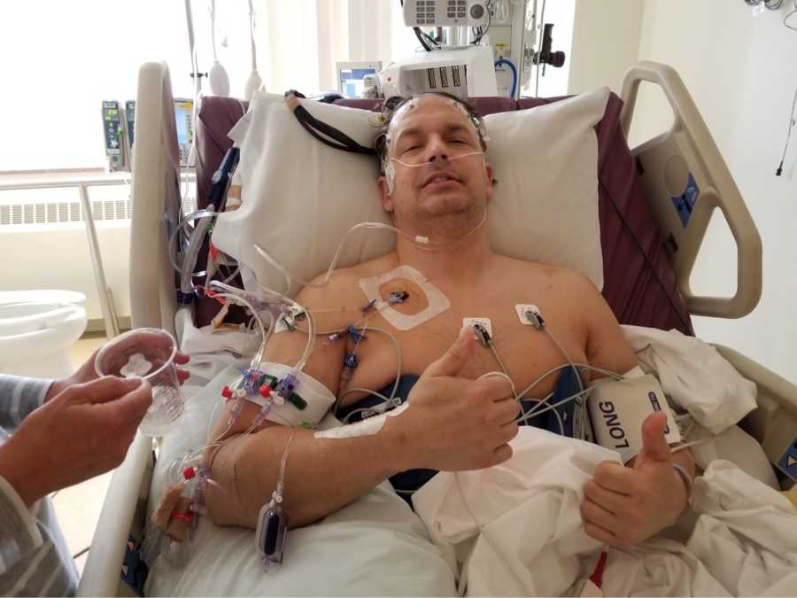 Man who went into cardiac arrest at gym lays in hospital bed with thumbs up