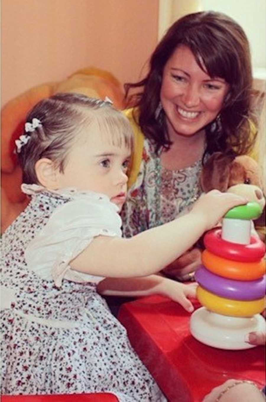 Woman smiles at her adopted Ukrainian daughter with down syndrome who is playing with toys