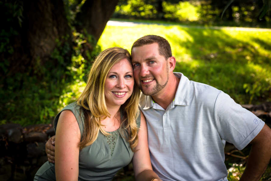 Husband and wife sit smiling outside in photoshoot