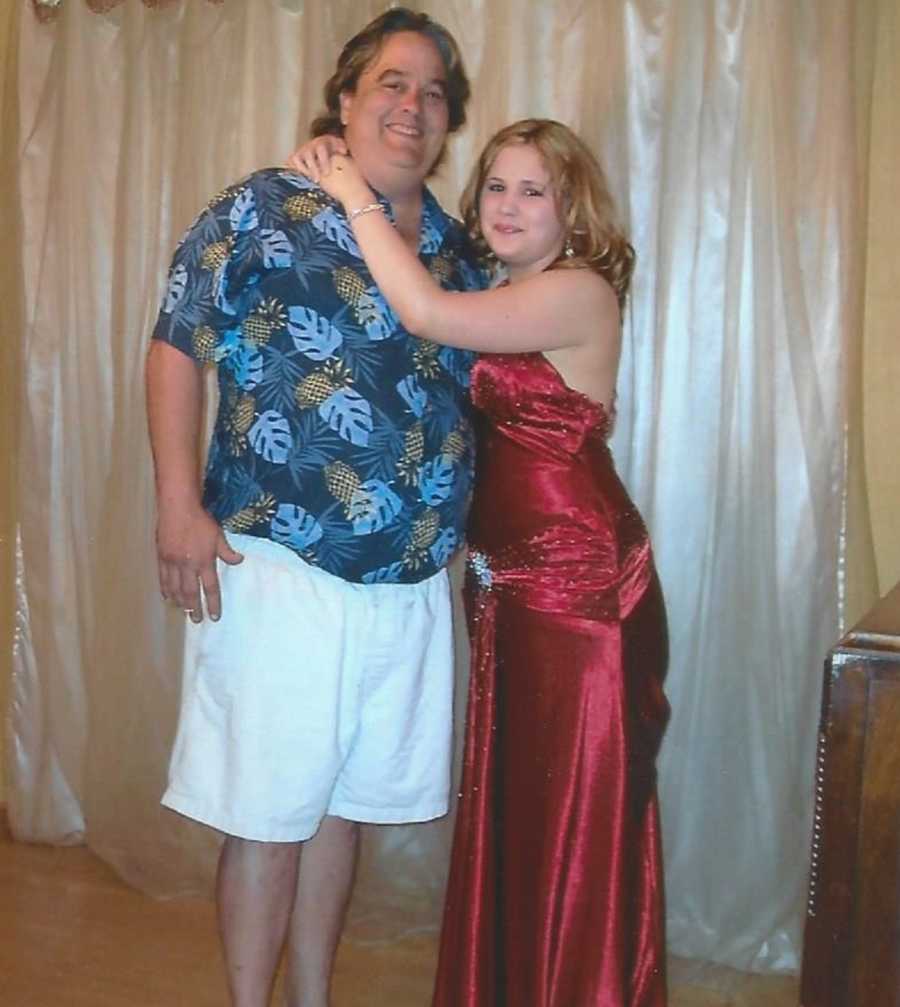 Young woman stands in red gown with arms wrapped around late fathers shoulders