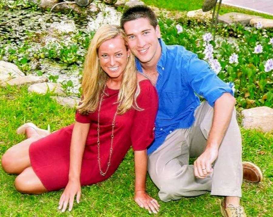 Young couple who struggle to get pregnant sit in grass smiling in front of flower patch