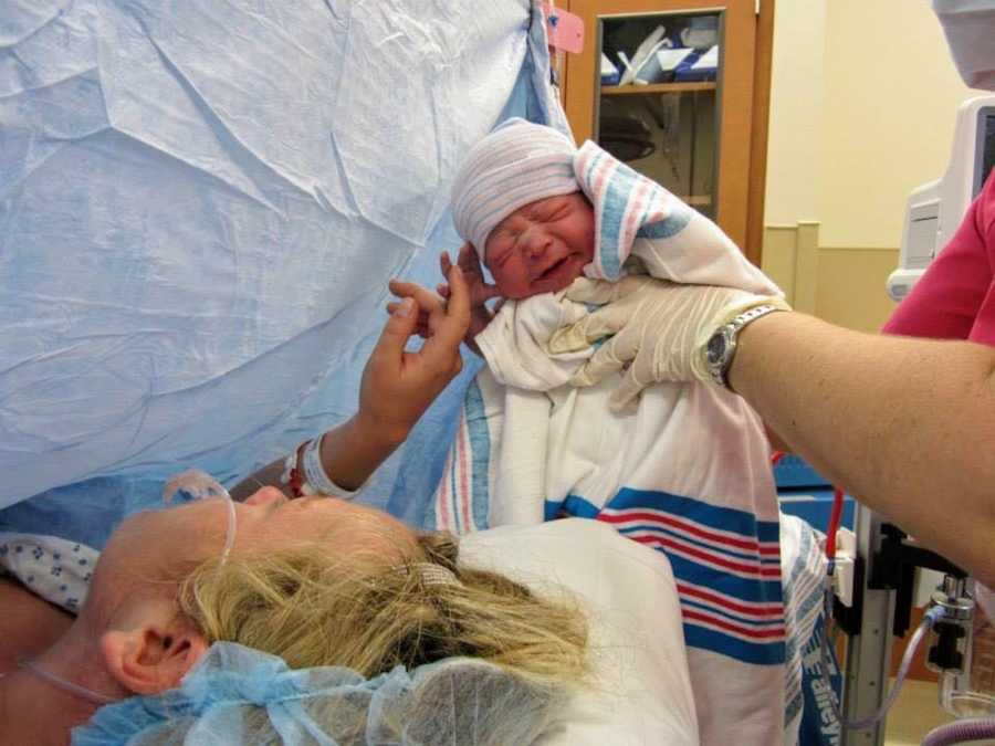 Nurse holds up newborn above mother's head who is laying on operating table after c-section