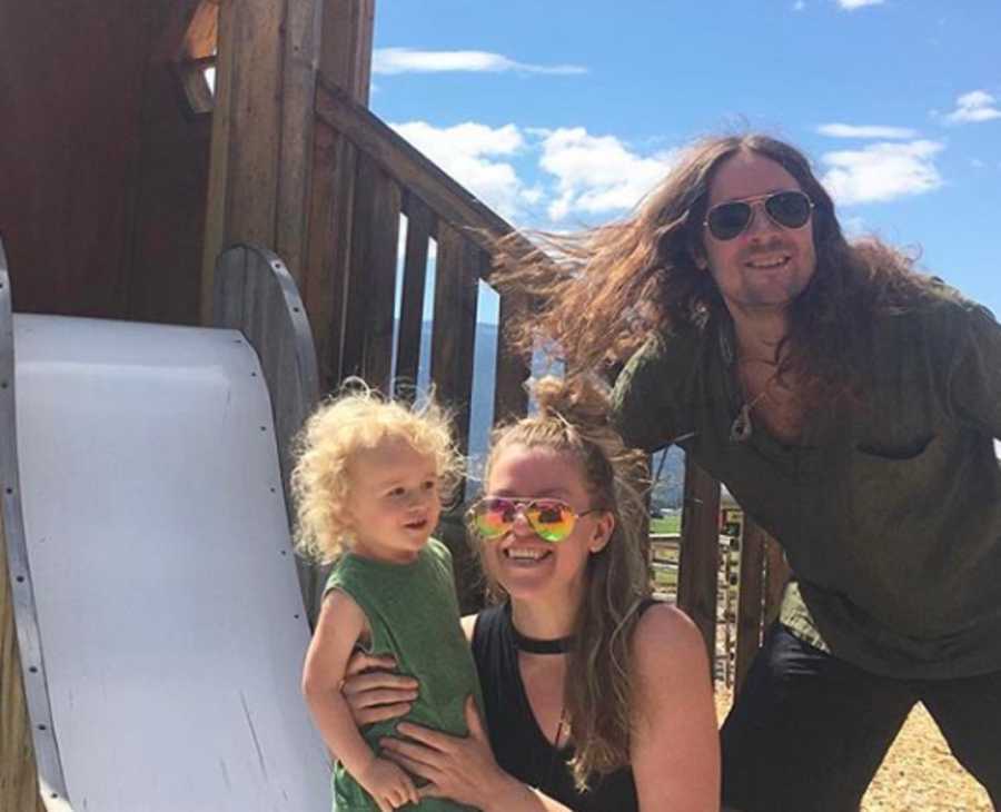 Mother and father smile with son beside play structure