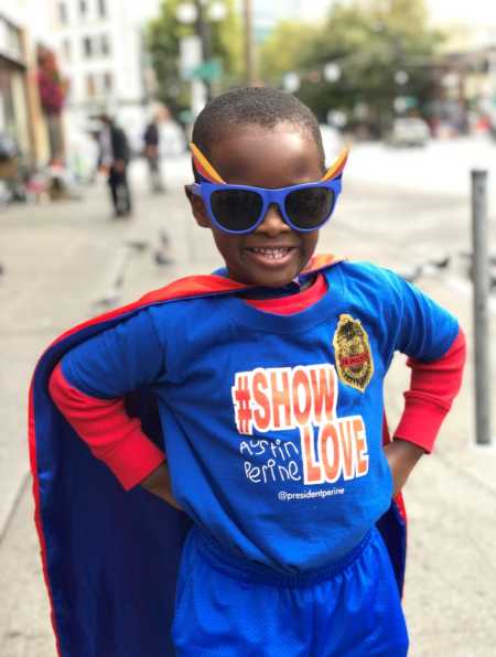 Young boy in sunglasses and cape wearing t-shirt that promotes non profit that supports homeless people