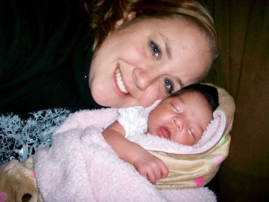 Mother smiles as she rests head on sleeping adopted baby