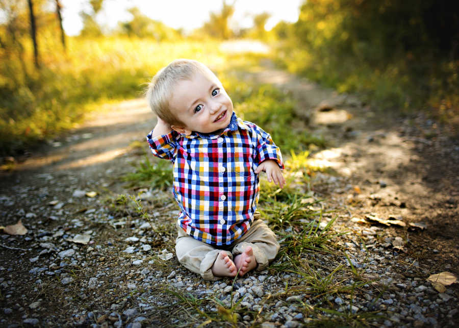 Little boy with dwarfism smiles as he sits on ground outside in photoshoot