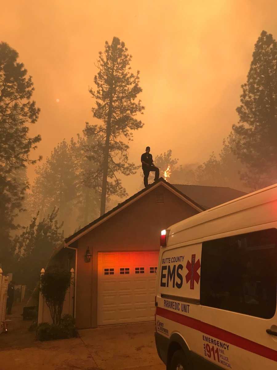 Fireman standing on top of garage roof with smokey air and trees in background