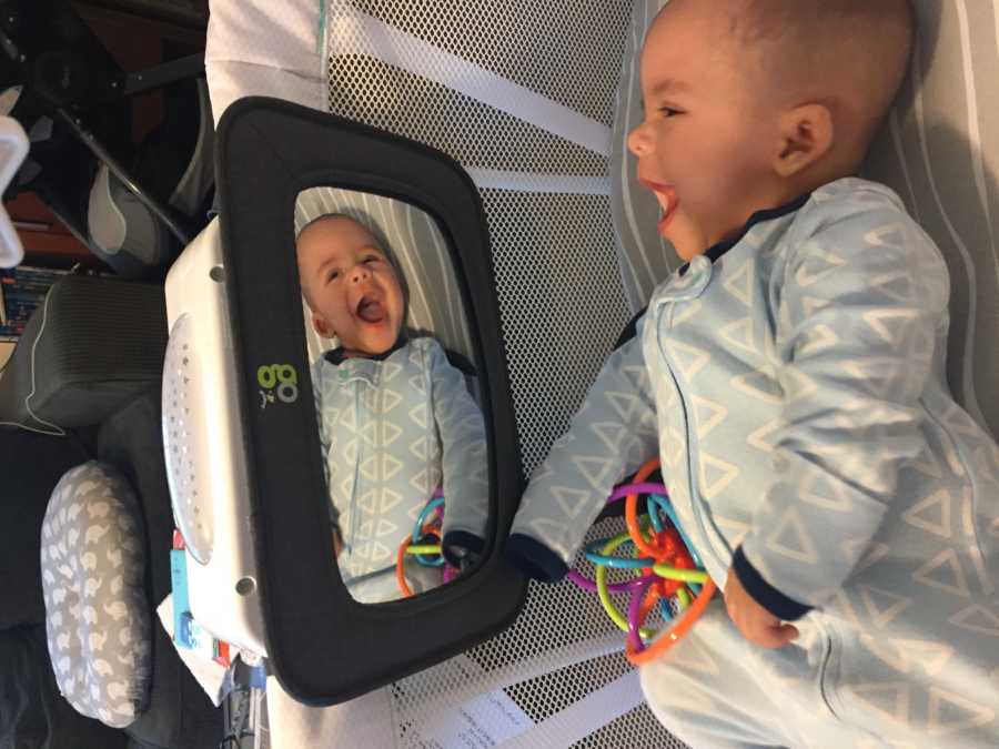 Baby with shaken baby syndrome smiles in crib as he looks at himself in mirror