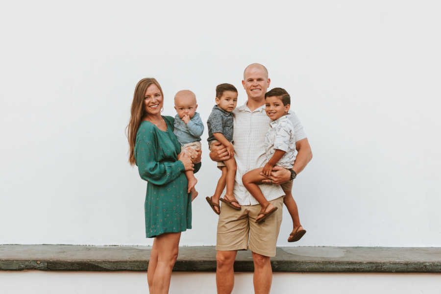 Husband stands holding two adopted sons beside wife who holds their biological son