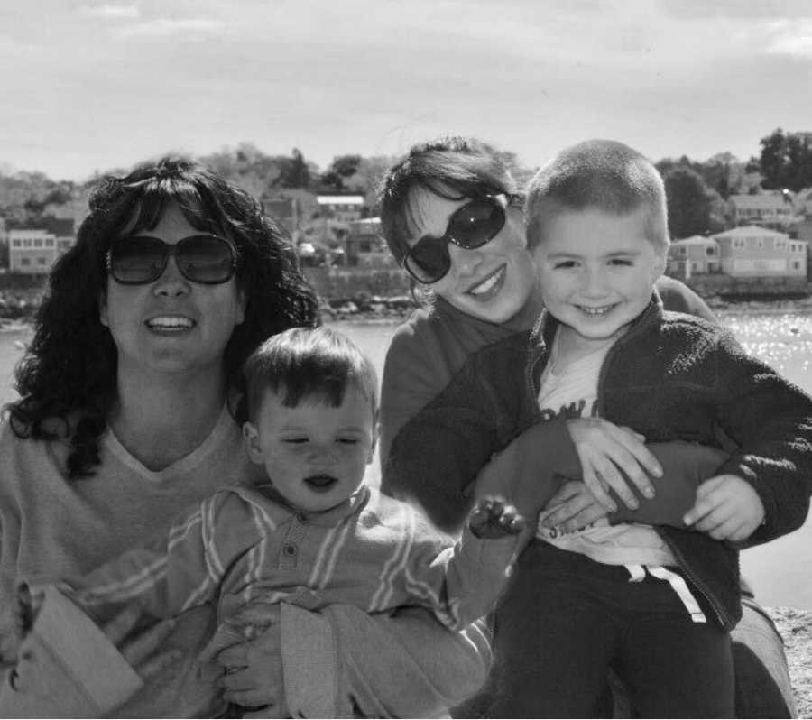 Woman smiles with child in her lap beside best friend with her own child in her lap