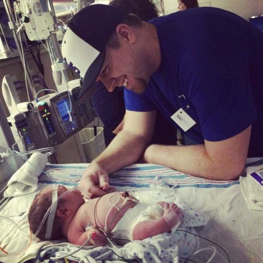 Father smiles as he leans over newborn son in NICU with dwarfism