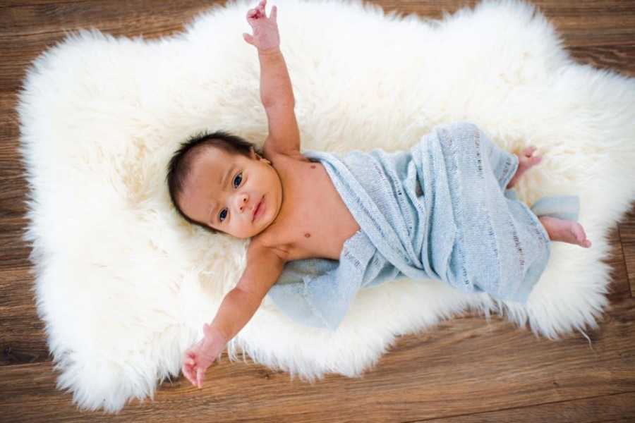 Baby lays on back of white fur blanket wrapped in blue blanket