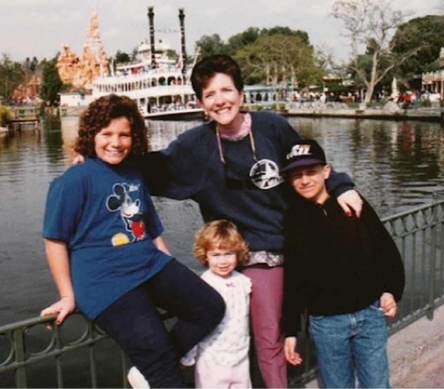 Young girl stands besides brother, mother and sister beside body of water