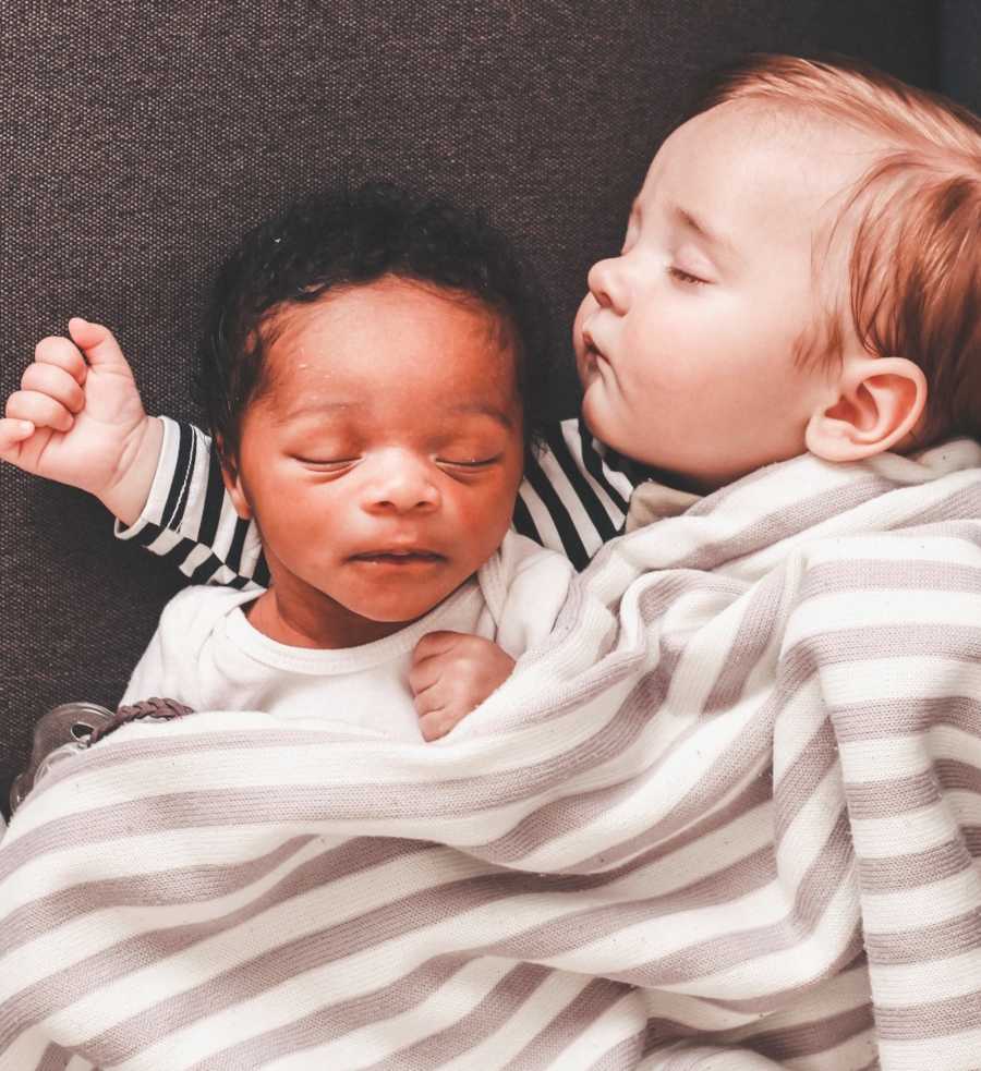 Newborn and adopted newborn lay asleep with blanket over them