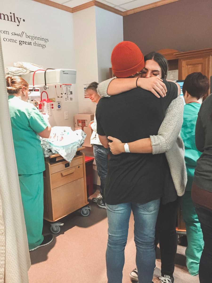 Husband and wife hug in hospital room beside their adopted newborn