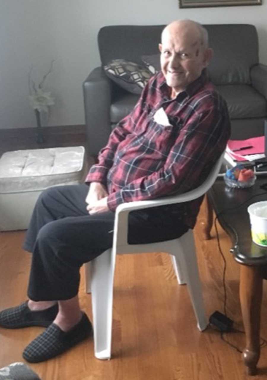 Elderly man who has since passed away smiles as he sits in plastic chair 