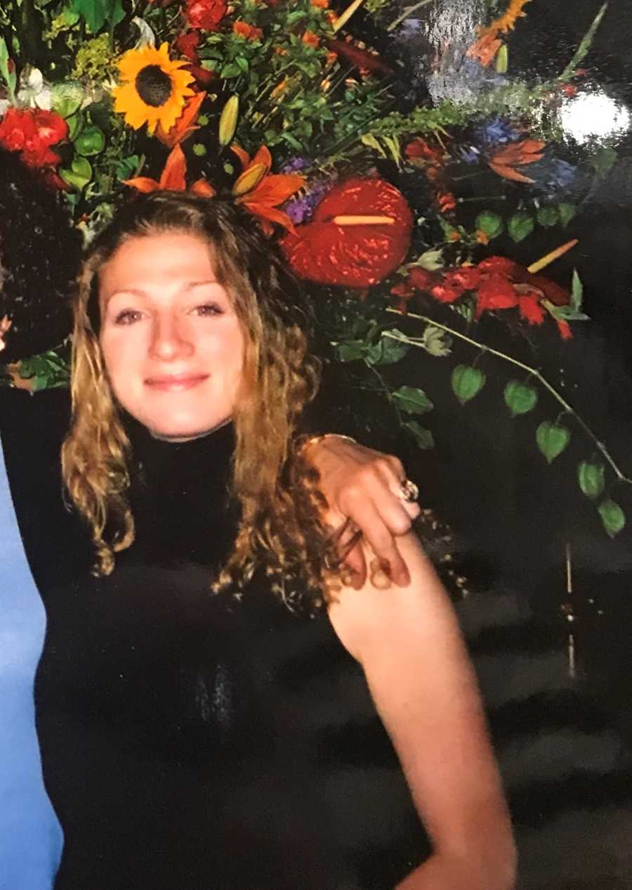 Woman in black dress smiling in front of bouquet of flowers who would one day be an alcoholic