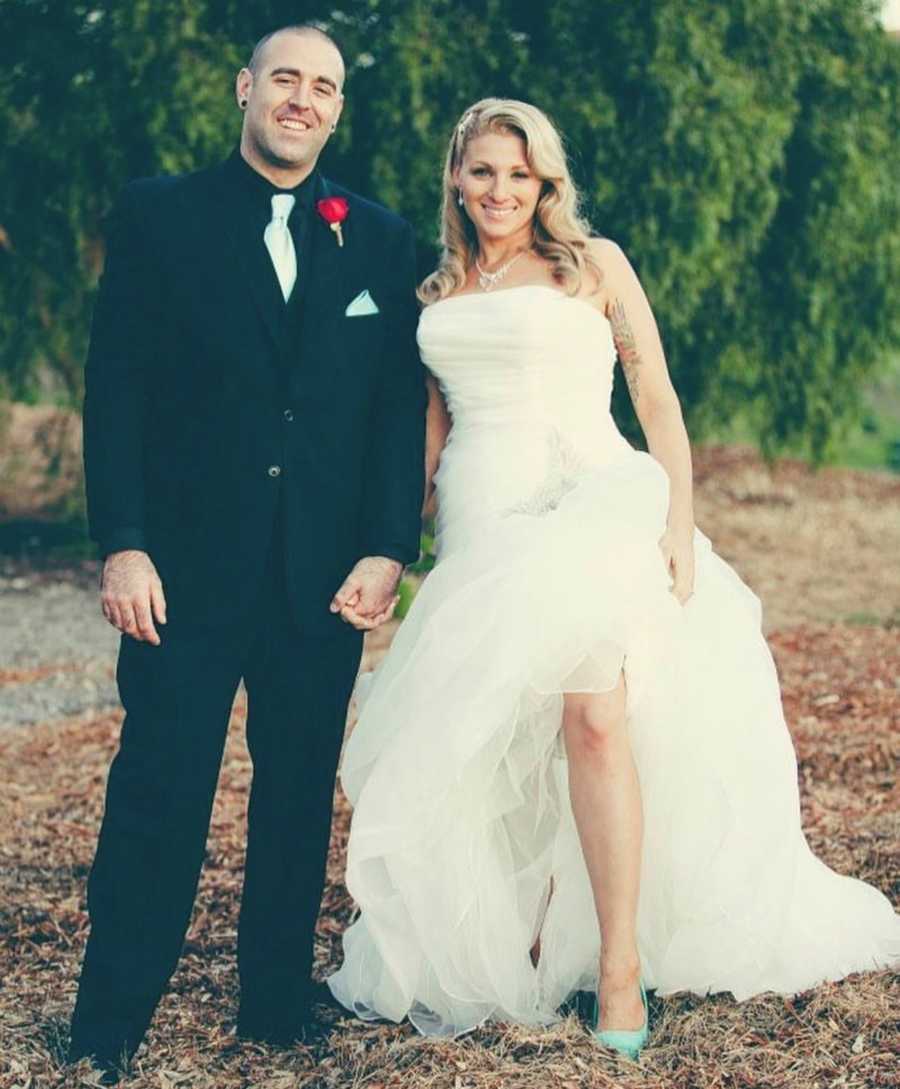 Sober bride and groom stand holding hands outside smiling