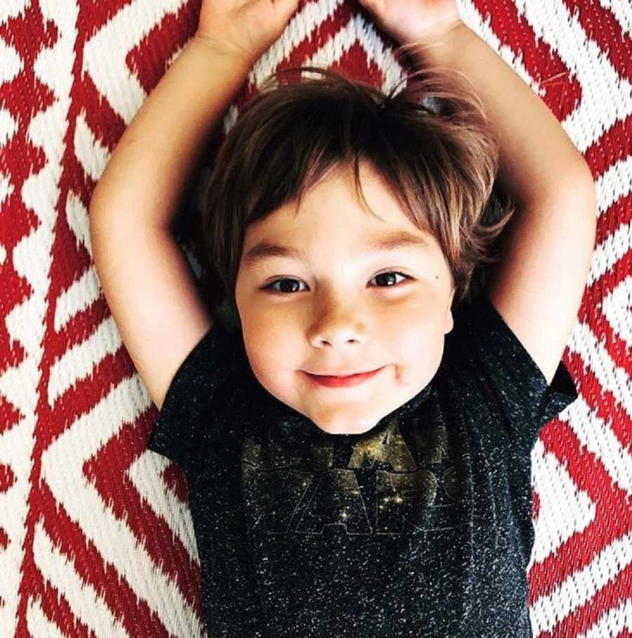 Young boy lays on his back with arms above his head smiling