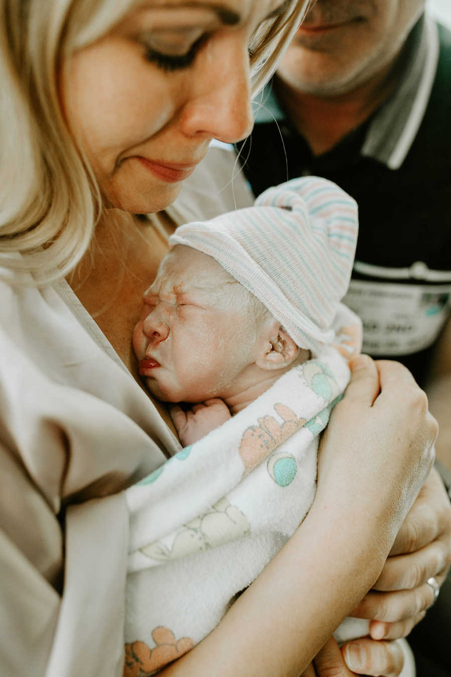 Mother smiles as she looks down at newborn that surrogate gave birth to