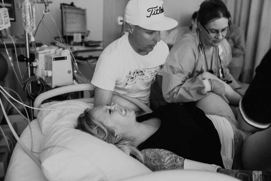 Surrogate in fetal position giving birth while her husband stands at her side