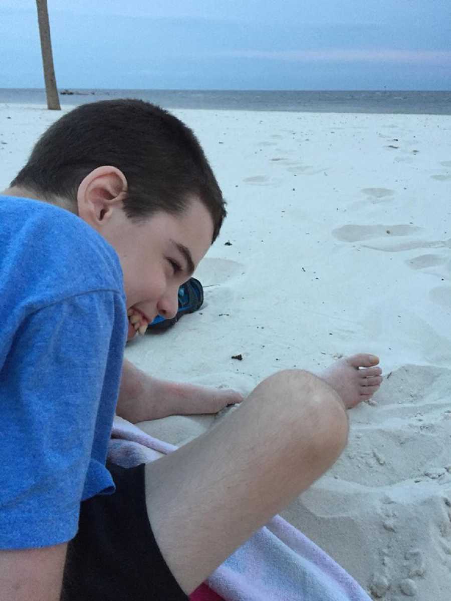 Teen with severe uncontrollable epilepsy sits smiling on beach
