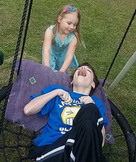 Teen with severe uncontrollable epilepsy lays on tree swing while his younger sister pushes him