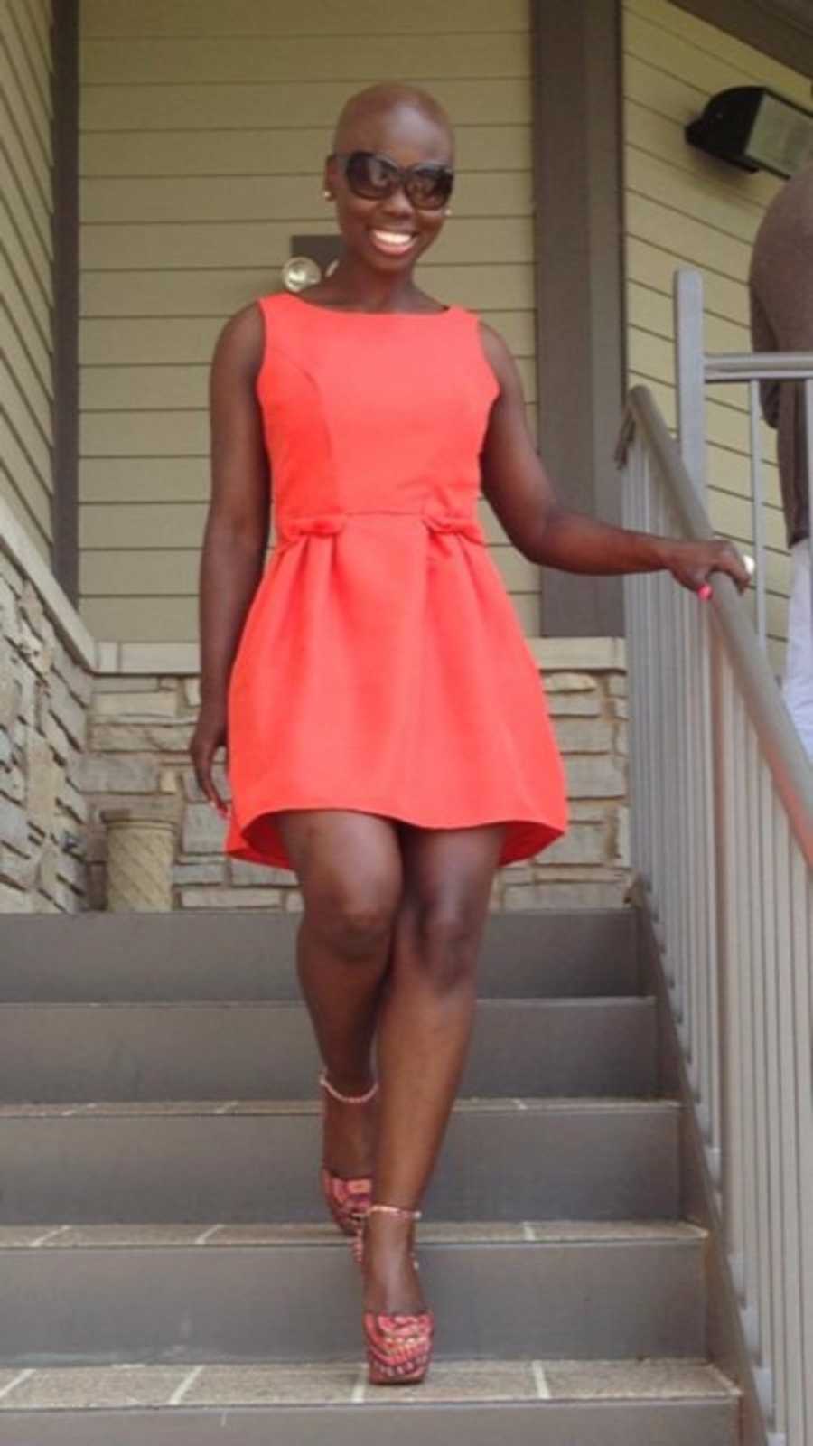Young woman with stage 2 cancer stands smiling on steps in orange dress