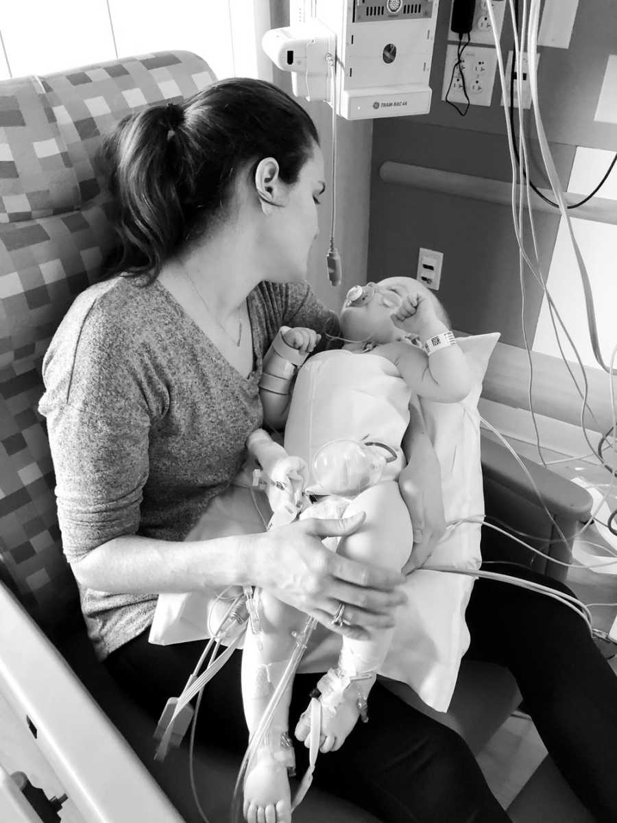 Mother sits in PICU holding baby in her lap who needs heart surgery