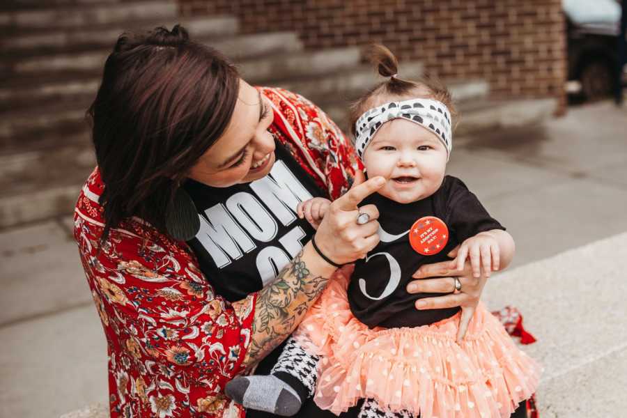 Foster mother sits outside on steps of adoption court with adopted daughter on her lap