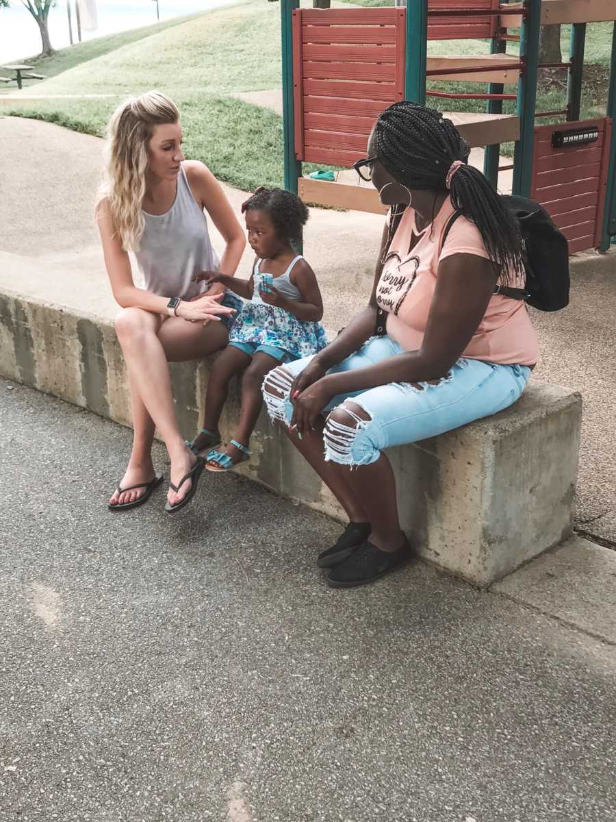 Mother sits on bench at playground with adopted daughter and her birth mother