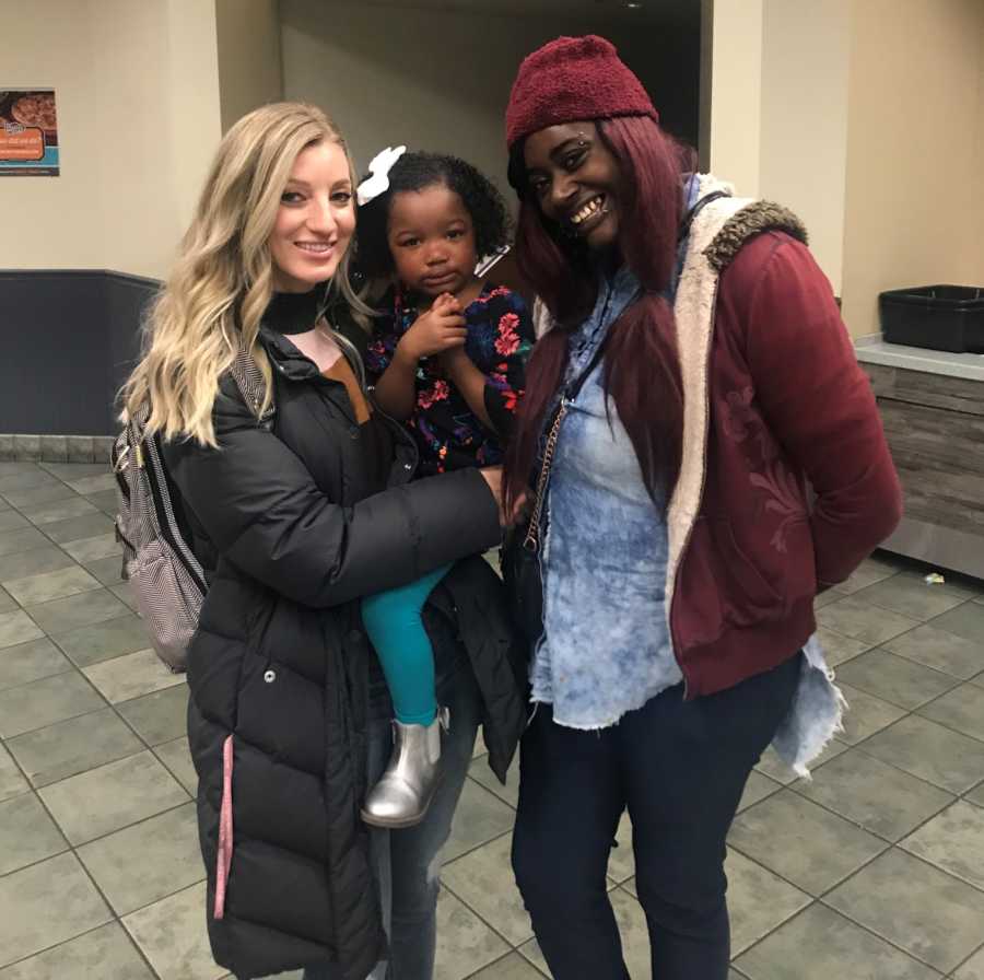 Mother stands holding adopted daughter beside daughter's birth mom