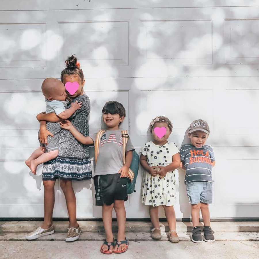 Husband and wife's three sons stand beside two foster girls in front of garage door